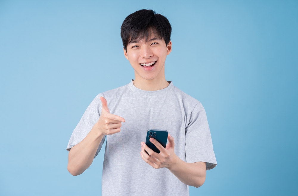 Young,Asian,Man,Using,Smartphone,On,Blue,Background